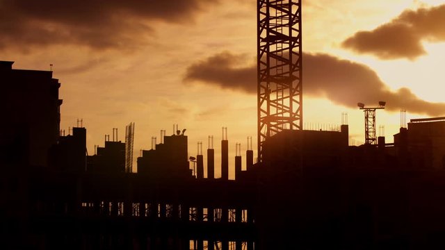 Silhouette of tower crane working on construction site elevate cement mixer, constructors working on residential building sunny evening, golden hour, warm cloudy sky
