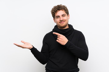 Blonde man over isolated white wall holding copyspace imaginary on the palm to insert an ad