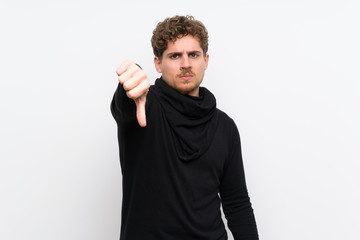 Blonde man over isolated white wall showing thumb down with negative expression