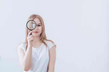 Girl with blond hair is holding a magnifying glass. Enlarged eye. Smile. Research search