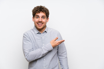 Blonde man over isolated white wall extending hands to the side for inviting to come