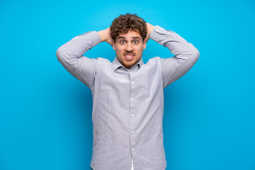 Naklejka premium Blonde man over blue wall frustrated and takes hands on head