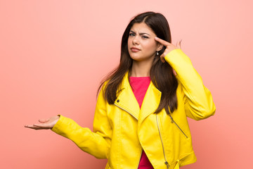 Teenager girl over pink wall making the gesture of madness putting finger on the head