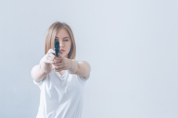 Young beautiful girl holding a gun in her hands. Aims at the camera.