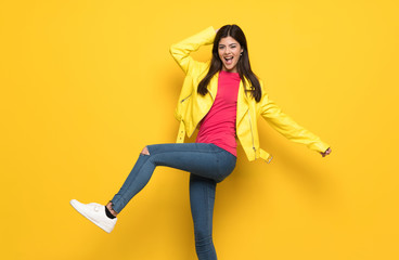 Teenager girl jumping over isolated yellow wall