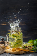 Detox water with lime, thyme and mint  in a mason jar against a dark wooden background. With splash