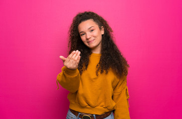 Teenager girl over pink wall inviting to come with hand. Happy that you came