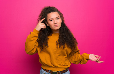 Teenager girl over pink wall making the gesture of madness putting finger on the head