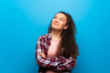 Teenager girl over blue wall looking up while smiling