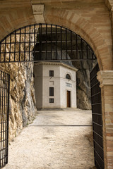 The first view of the church in the cave known as Temple of Valadier, seen through an metal gate and stone archway. The church is unique in that it is tucked into a cave over the looking the valley.