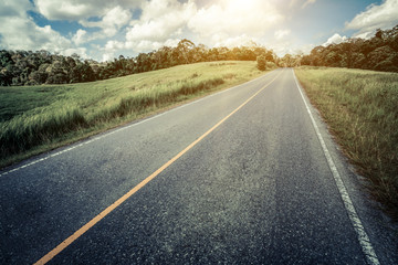 Highway road up hill through green grass field under white clouds on blue sky in summer day. Road...