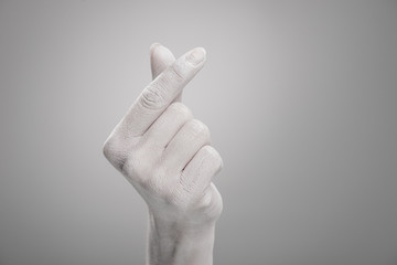 cropped view of female hand painted in white showing heart-shaped sign on grey