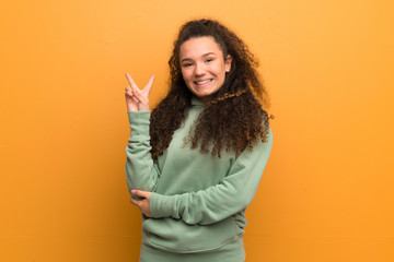 Teenager girl over ocher wall smiling and showing victory sign