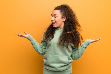 Teenager girl over ocher wall holding copyspace with two hands