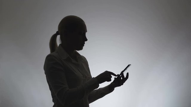 Silhouette of a woman on a white background. A woman writes a message in the phone. Woman uses the internet in a smartphone.
