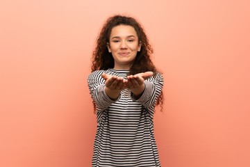 Teenager girl over pink wall holding copyspace imaginary on the palm to insert an ad