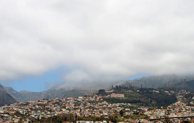Fototapeta na wymiar a panoramic view of funchal in madeira with houses between green hills and the mountains under white cloud