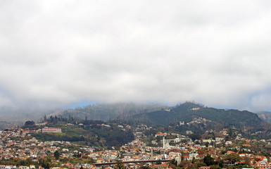 Fototapeta na wymiar a panoramic view of the city of funchal with buildings and road bridge with mountains covered by white misty cloud