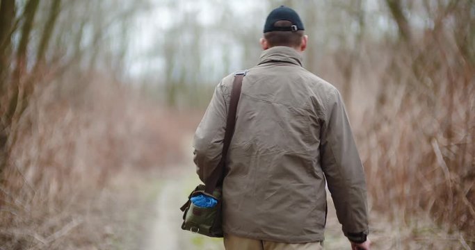 Man Holding Fishing Rod Walking Amidst Bare Trees