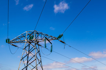Top segment of a high voltage steel power tower or pylon with green glass line suspension insulators against a blue sky background.