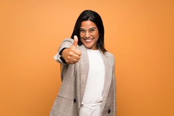 Young Colombian girl over brown wall with thumbs up because something good has happened