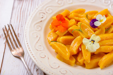 Tasty yellow pumpkin gnocchiwith spinach and parmesan cheese on a plate closeup. Decorated with edible flowers