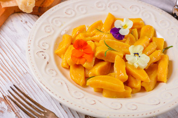 Tasty yellow pumpkin gnocchiwith spinach and parmesan cheese on a plate closeup. Decorated with edible flowers