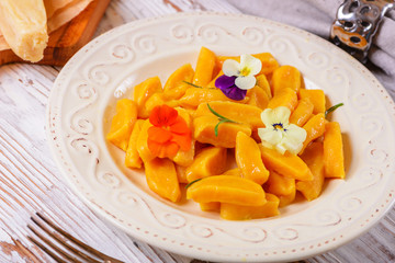 Tasty yellow pumpkin gnocchiwith spinach and parmesan cheese on a plate closeup. Decorated with edible flowers