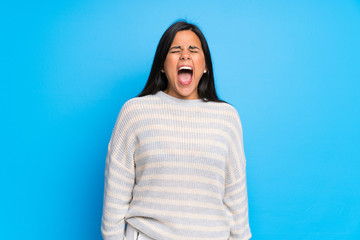 Fototapeta premium Young Colombian girl with sweater shouting to the front with mouth wide open
