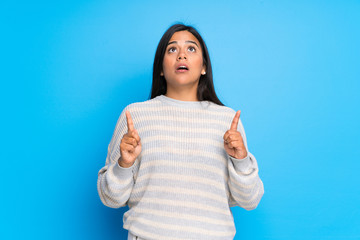 Young Colombian girl with sweater surprised and pointing up