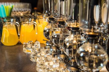 Fototapeta na wymiar Elegant vacuum glass siphon and blurry orange drinks with slices of orange fruit inside big glass bowls in background. Drinks served on table ready for holiday celebration. Horizontal color photo.