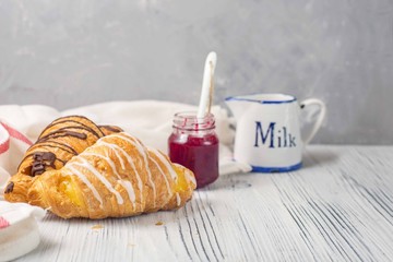 Fresh croissants with jam for breakfast on old white wooden background