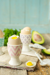 Boiled eggs in holders with avocado on a grey wooden rustic table