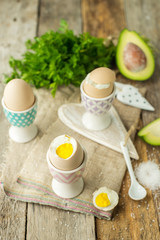 Boiled eggs in holders with avocado on a grey wooden rustic table