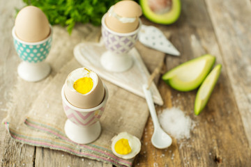 Boiled eggs in holders with avocado on a grey wooden rustic table