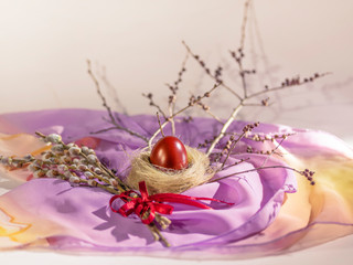 red Easter egg in a nest, willow twigs tied with a red ribbon against the background of twigs. The whole composition on a color napkin.