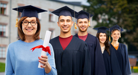 graduation, education and old age concept - happy senior graduate student woman in mortar board with diploma next to young people over university campus background