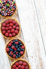 Raspberry and blueberry tartlets with chocolate ganache, fresh berries and mint leaves, selective focus. Fresh fruit tart on white background, freshly homemade fruit cake on a table