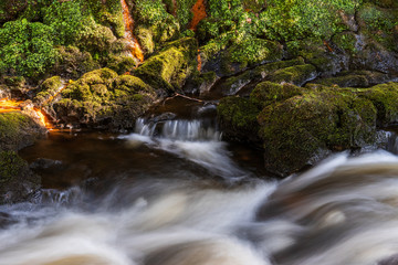 Long exposure of a river flowing through moss covered rocks. Dodder river landscape in Kiltipper Park, Dublin, Ireland.