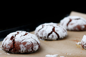 Chocolate cookies with cracks on baking paper and iolated on black. Cracked chocolate biscuits