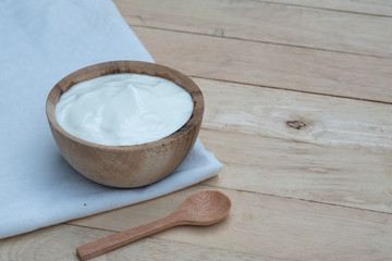 Natural homemade plain organic yogurt in wooden bowl and wood spoon on wood texture background