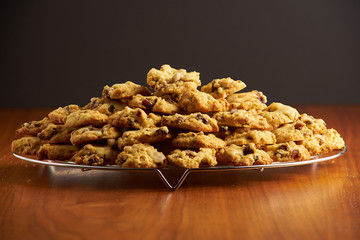 Stack of cookies on a metal cooling grid placed on a wooden surface with black background 