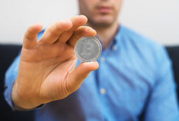 Man holding silver physical bitcoin. Symbol of virtual currency.