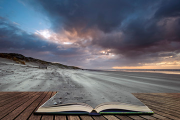 Stunning Winter sunrise over West Wittering beach in Sussex England with wind blowing sand across the beach in pages of open book, story telling concept