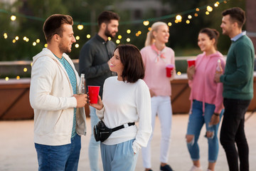 leisure, celebration and people concept - happy friends with drinks in party cups toasting at rooftop