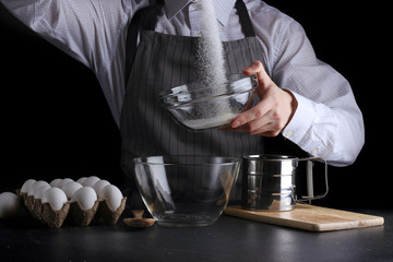man pouring sugar in bowl on black background. pie making concept