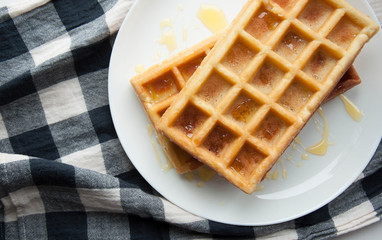Belgian waffles on a white plate on the table. French or American breakfast. Vintage style. Sweet food.