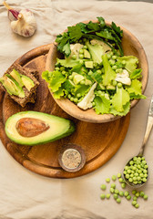 Fresh delicious green salad with avocado in a wooden plate and gluten free toast. Top view. Healthy lunch dish and Diet detox food concept.