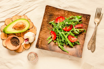 Fresh light green salad with avocado and tomatoes in a wooden plate. Top view.