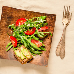 Fresh light green salad with avocado and tomatoes in a wooden plate. Top view.